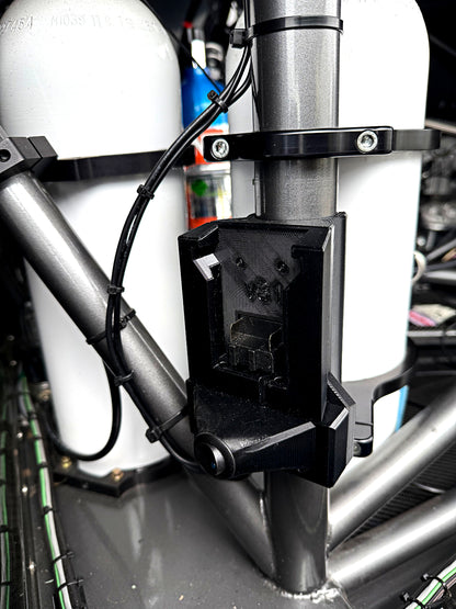A close-up of a black plastic mounting bracket attached to a silver metal frame, with white cylindrical tanks and black wiring visible in the background.