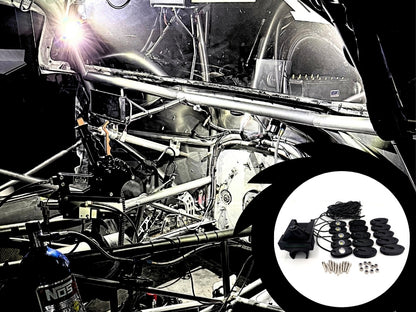 A black aftermarket car audio speaker kit with multiple round black drivers, a central black speaker, and mounting hardware, shown in a circular inset overlay against a background of a stripped race car frame with a bright welding light.