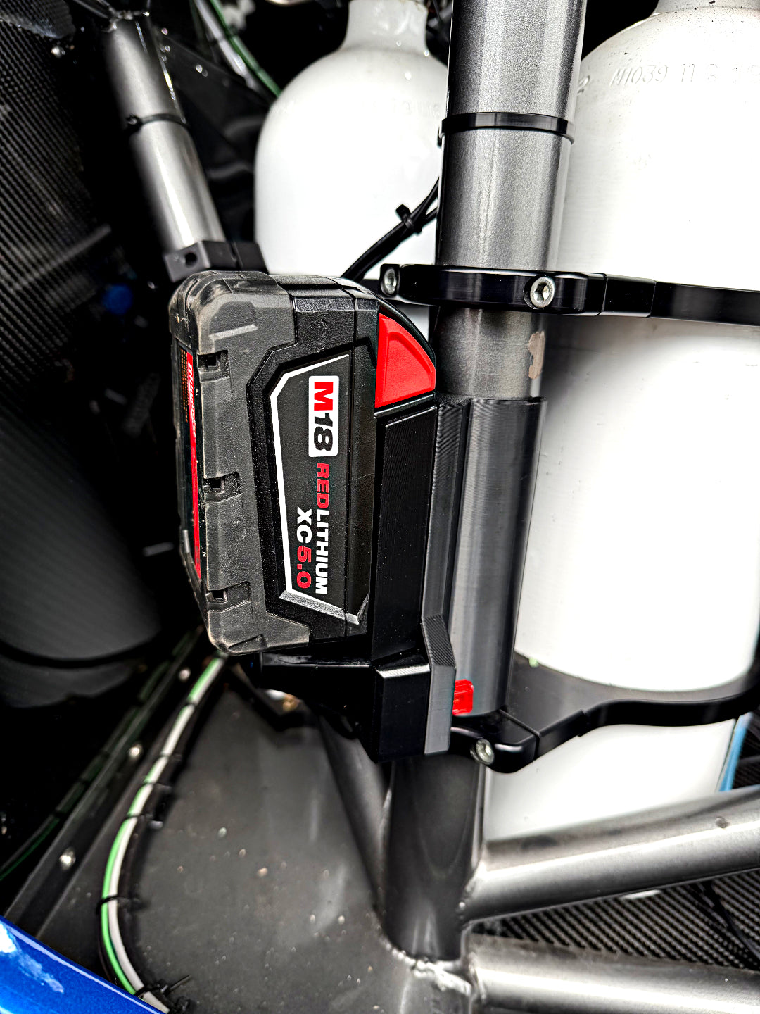 A close-up of a black and red M13 Ecbl Lithium XC 500 battery mounted on a metallic frame next to white cylindrical tanks.