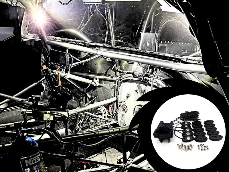 A black aftermarket car audio speaker kit with multiple round black drivers, a central black speaker, and mounting hardware, shown in a circular inset overlay against a background of a stripped race car frame with a bright welding light.